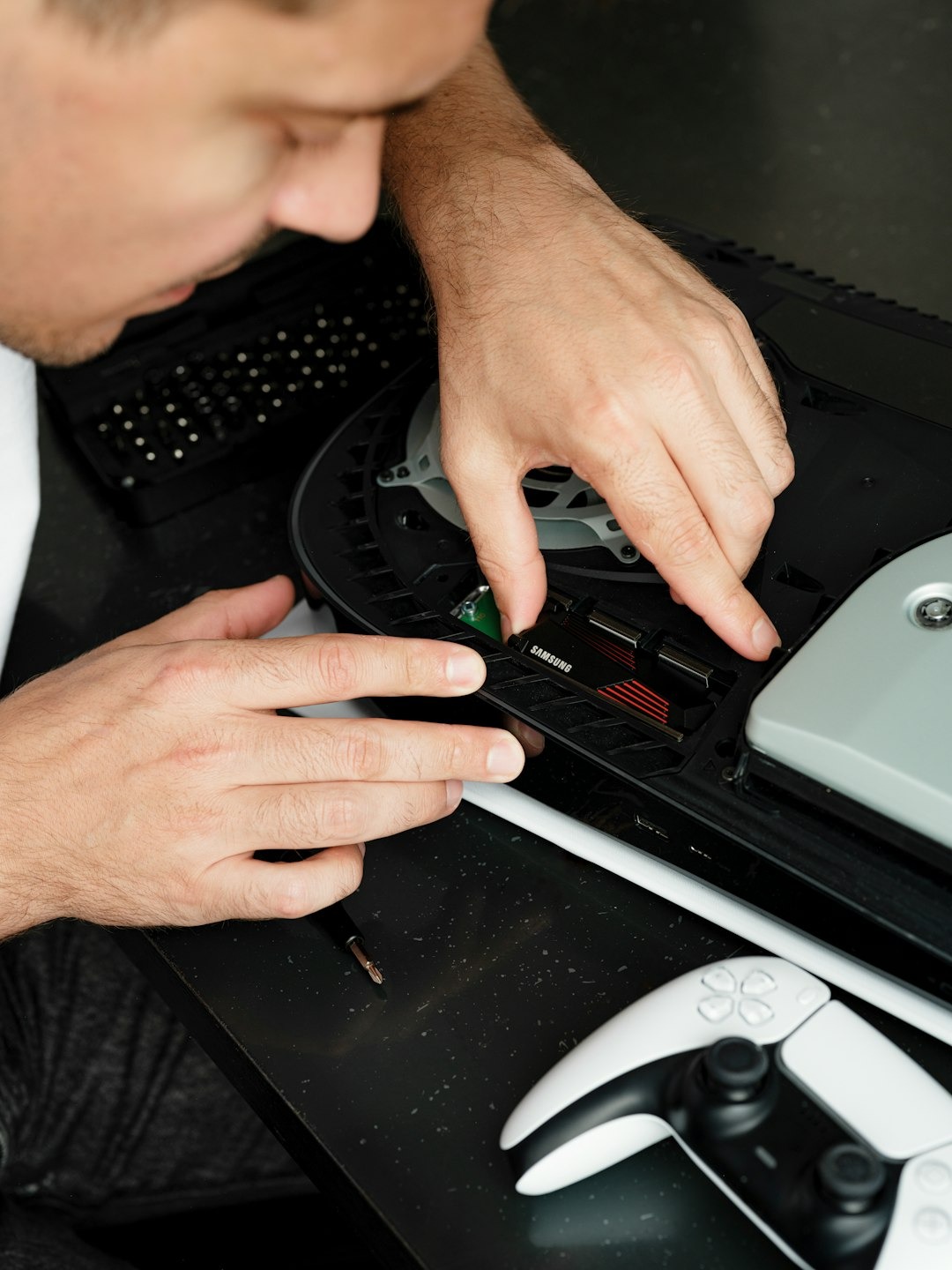 Man's hands installing a black storage component into a game console.